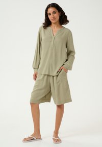 Bluză verde deschis, cu mânecă lungă, cu nasturi, asortată cu pantaloni scurți până la genunchi. Material moale, texturat, cu buzunare laterale și croială lejeră.