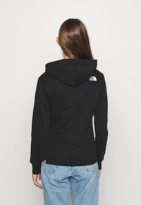 Svart hoodie i bomullsblandning, med en känguruficka och vitt logotyp på baksidan. Den har en dragskohuva och ribbad nederkant.