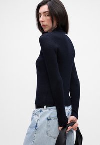 Námornícky pletený sveter s dlhými rukávmi a vysokým golierom, kombinovaný s svetlomodrými džínsami. Minimalistické a textúrované povrchy.