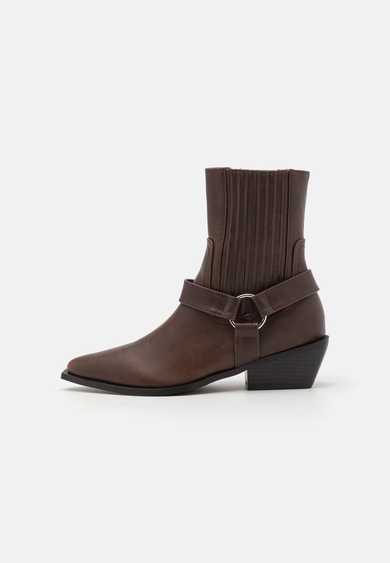 Botte brune en cuir à cheville avec bout pointu, talon bas empilé, tige en maille élastique côtelée et sangle décorative avec anneau en métal.