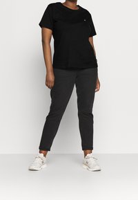 Černé bavlněné tričko s krátkými rukávy a kulatým výstřihem, v kombinaci s tmavě šedými slim-fit kalhotami a bílými teniskami s šedými akcenty.