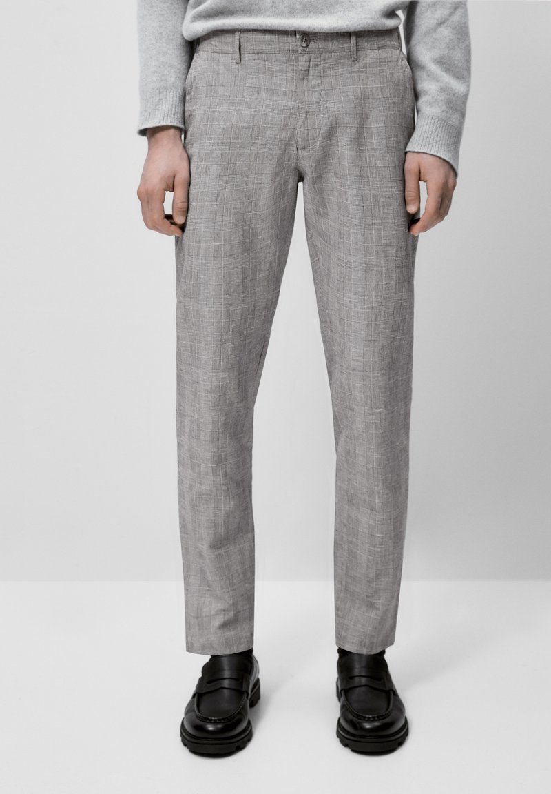 Pantaloni grigi chiari a disegno con una vestibilità su misura, caratterizzati da un sottile motivo a quadri. Realizzati in tessuto liscio, abbinati a scarpe nere.