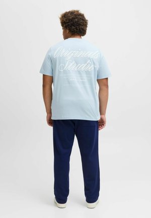 Light blue cotton t-shirt with white graphic text on the back, paired with navy sweatpants. Smooth texture, short sleeves, relaxed fit.