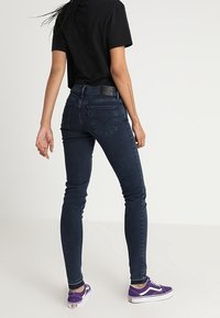 Mörkblå skinny jeans i denim, med medelhög midja, bakfickor och fransad fåll, kombinerade med lila sneakers och en svart t-shirt.