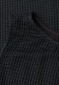Haut noir sans manches en tissu tricot gaufré texturé avec col rond, présenté plié sur une surface texturée assortie.