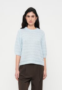 Ανοιχτό μπλε πουλόβερ πλεκτό με ανάγλυφο σχέδιο, στρογγυλή λαιμόκοψη και κοντά μανίκια, σε συνδυασμό με σκούρο καφέ παντελόνι ψηλόμεσο.