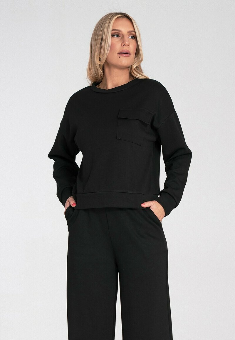 Czarny sweatshirt z długimi rękawami, okrągłym dekoltem i przednią kieszenią. Miękka tkanina i luźny krój. Połączony z dopasowanymi czarnymi spodniami.