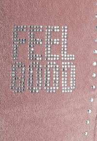 Roze stof met de tekst "FEEL GOOD" in zilveren rhinestones, met extra zilveren studs langs de rand voor versiering.