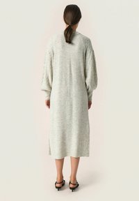 Abito lungo grigio in maglia con una vestibilità ampia, caratterizzato da maniche in maglia a treccia testurizzata e spacchi laterali, realizzato in materiale morbido e leggero.