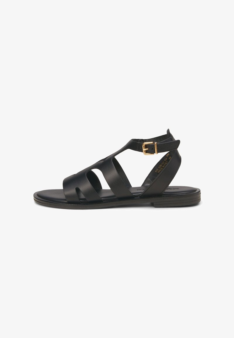 Sandales noires avec design découpé, bride de cheville réglable avec boucle dorée, semelle plate et texture lisse. Style classique de chaussures d'été.
