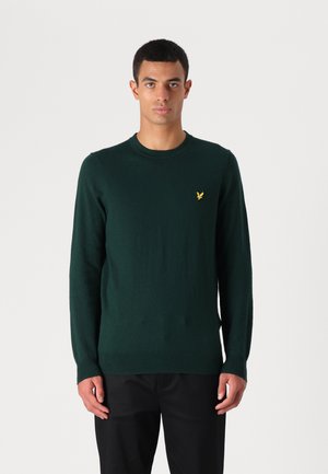 Maglione verde lavorato a maglia con maniche lunghe e scollatura rotonda. Presenta un piccolo logo giallo sul petto. Texture morbida, design aderente.