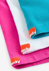 Tre sammenfoldede t-shirts i turkis, hvid og pink bomuld med orange "nerdede" mærker ved sømmen. Glat tekstur og rene syningsdetaljer.