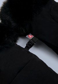 Czarna pikowana kurtka z czarnym kołnierzem z futerka ekologicznego, wyposażona w czerwoną naszywkę z logo oraz zapięcie na plastikową klamrę. Gładka faktura, ocieplana konstrukcja.