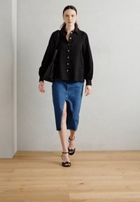 Black striped button-up shirt, blue denim midi skirt with front slit, black strappy sandals, and shoulder bag, set against a neutral background.