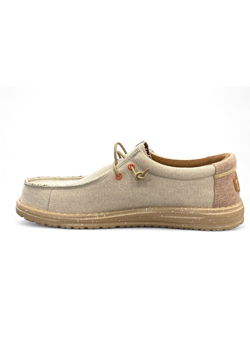 Zapato slip-on de lona beige con detalles en marrón, que presenta una superficie texturizada, suela de goma y cordones ajustables. Detalles de entresuela moteada.