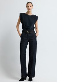 Černý bezramínkový top se strukturovaným designem a jemnou výzdobou na výstřihu, spojený s tmavými džínovými kalhotami s širokými nohavicemi.