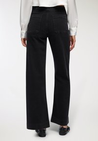 Czarne dżinsy o szerokich nogawkach, wykonane z denimu, z wysokim stanem, dwoma tylnymi kieszeniami i widocznym przeszyciem przy końcu nogawki. W połączeniu z bluzką.