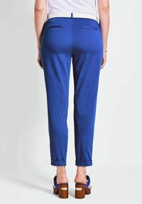 Koninklijk blauwe broek met een getailleerde pasvorm, voorzien van een witte tailleband, achterzakken en omgeslagen pijpen, gecombineerd met bruine platformhakken.