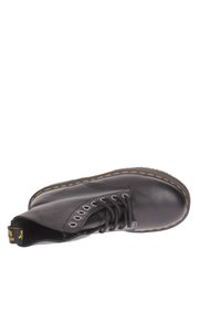 Botte en cuir noir avec une pointe ronde, des coutures jaunes, sept œillets et un design à lacets. Texture lisse avec un léger éclat.