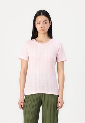 T-shirt en tricot rose clair avec une texture côtelée et des manches courtes, associé à un pantalon vert plissé. Encolure ronde simple.