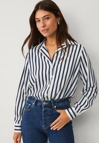 Marineblauw en witte gestreepte blouse met kraag, lange mouwen en manchetdetail, gecombineerd met hoge blauwe spijkerbroek.