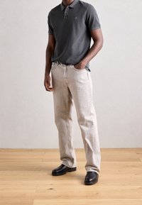 Šedá polo košile s límečkem, světlé béžové rovné džíny a černé slip-on boty. Hladká tkanina, uvolněný střih, kontrastní švy.