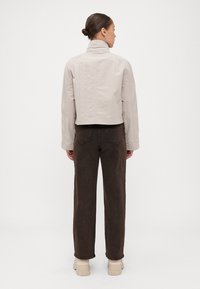 Cropped, light grey jacket with high collar and long sleeves, paired with dark brown straight-leg pants and beige sneakers.