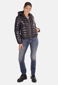 Giacca a piuma nera con design aderente, cuciture orizzontali, chiusura con zip e cappuccio attaccato, abbinata a jeans blu e stivali neri.