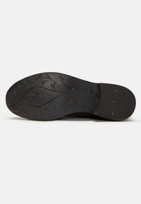 Suela de zapato negra con patrones texturizados, tacón plano y diseños en relieve. Material de goma duradero con detalles de costura visibles.