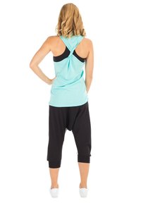 Een turquoise tanktop met een gedraaide rugontwerp, gedragen over een zwarte sportbh, gecombineerd met zwarte capri-broeken met een laag kruis en witte sneakers.