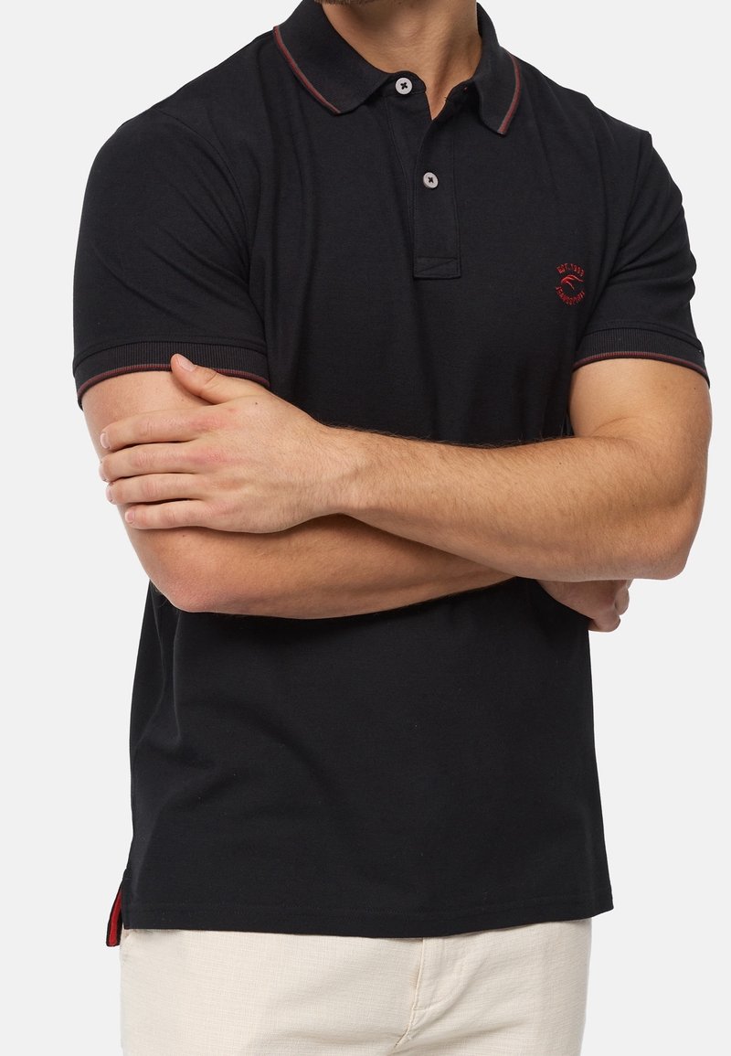 Polo-shirt noir en coton, avec un accent rouge sur le col et les manches, une patte de boutonnage et un petit logo sur la poitrine.