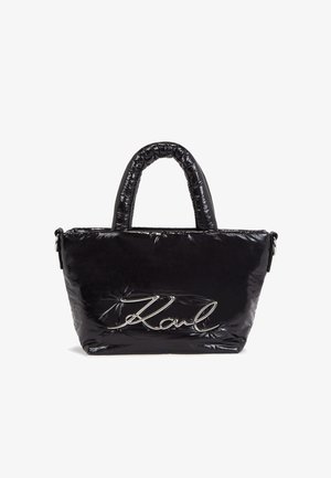 Sort skinnende tote taske med polstrede håndtag og sølvskrift "Karl" logo foran, stående opret på hvid baggrund.