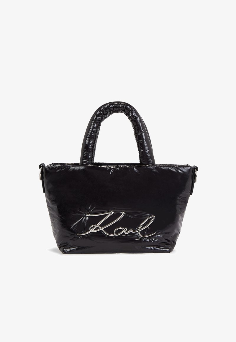 Sac cabas noir brillant avec poignées rembourrées et logo "Karl" en écriture argentée sur le devant, debout sur fond blanc.