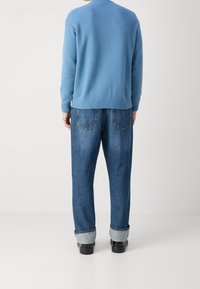 Ljusblå stickad tröja med ribbat avslut, i kombination med löst sittande mörkblå jeans med upprullade fållar och bakfickor.