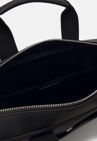Schwarze, strukturierte Laptoptasche mit einem Reißverschlussöffnung, Innenfächern und stabilen Griffen. Der glatte Innenstoff bildet einen Kontrast zur Außenseite.