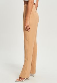 Beige op maat gemaakte broeken met een hoge taille, rechte pijpen, zachte stof en zijnaaddetails, gecombineerd met open teen hakken.