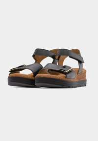 Zwarte leren sandalen met twee verstelbare banden, voorzien van een kurken sleehakzool en een rubberen buitenzool voor grip. Accenten van goudkleurig metaal.