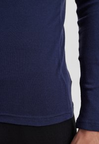 Navy langærmet skjorte lavet af blødt materiale, med en tætsiddende pasform og synlige sømme langs kanten og ærmeender.