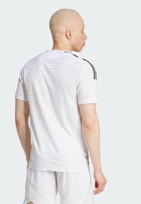 Camiseta de fútbol blanca de manga corta con un patrón texturizado, acentos negros en los hombros y un dobladillo ligeramente curvado. Adecuada para ropa deportiva.