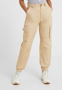 Beige cargo broeken met elastische boorden, voorzien van zijzakken, een knoopsluiting en gemaakt van duurzame stof.