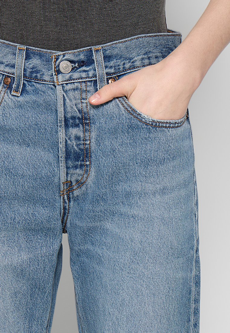 Jeans in denim azzurro chiaro con vestibilità rilassata, design a cinque tasche, cuciture arancioni in contrasto e una leggera texture sbiadita.
