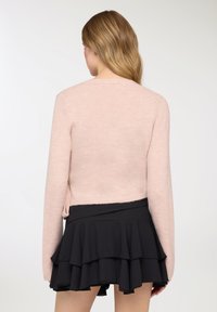 Maglione corto rosa chiaro con maniche lunghe, abbinato a una gonna nera a balze stratificate. Tessuto morbido e design semplice.