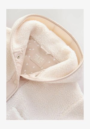 Veste en polaire couleur crème à l'intérieur, doublée d'un matériau doux et ornée d'un motif à pois. Inclut une étiquette de marque et une fermeture à pression.