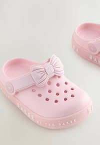 Rozā gumijas klumpi ir ar lielu loku akcentu uz siksniņas, ventilācijas caurumiem sānos un teksturētām zolemi ar "BAKER" zīmolu.