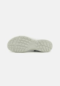 Suela de zapatilla gris claro con un patrón de textura y relieve para tracción, con una zona del talón suave y un detalle de marca sutil.