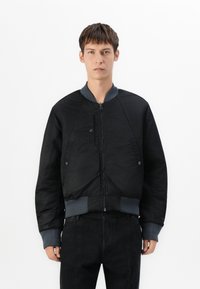 Giacca bomber nera con zip frontale, polsini e orlo a coste. Presenta una finitura testurizzata e tasche laterali, completata da un colletto grigio.
