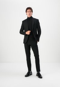 Black tailored suit with slim-fit trousers and a matching black turtleneck. Accessories include shiny black dress shoes. Minimalist design.