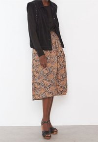 Veste en velours côtelé noir avec boutons-pression portée sur une jupe midi à motifs dans des tons orange et marron, associée à des sandales plateformes noires.