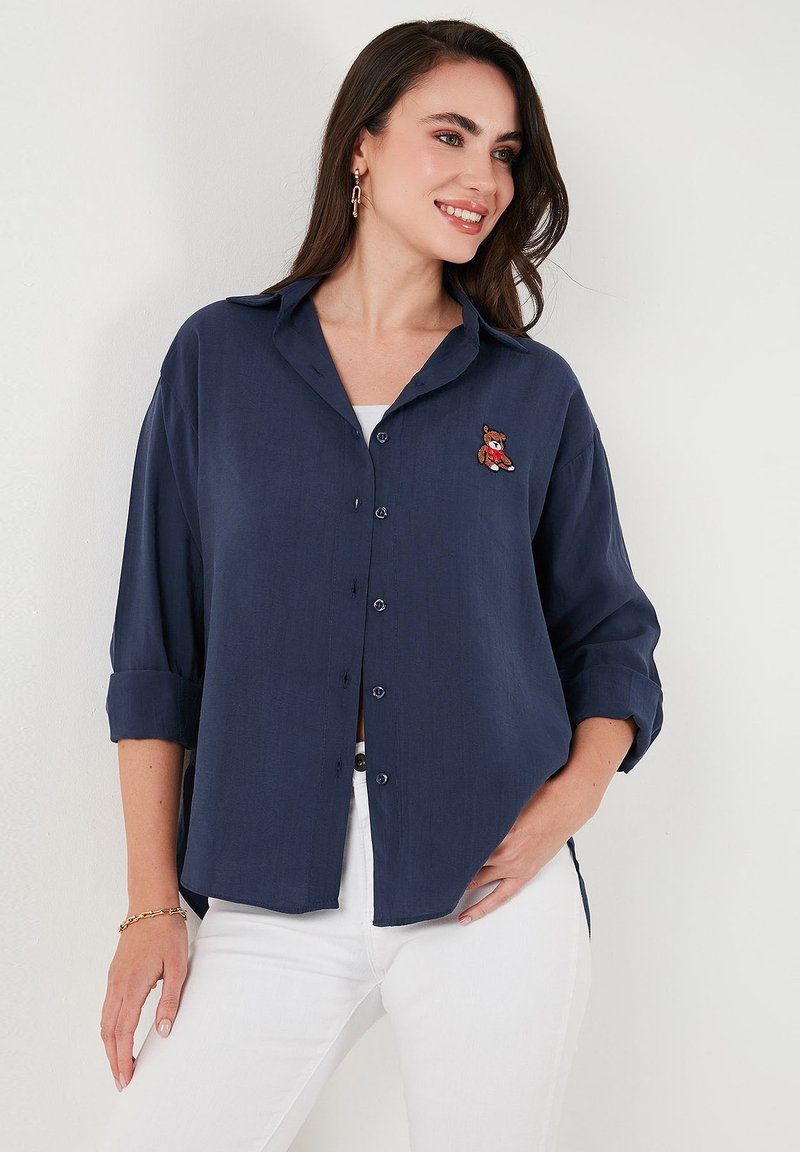 Navy blue button-up shirt with a relaxed fit, featuring rolled sleeves and an embroidered bear on the left chest. Made of lightweight fabric.
