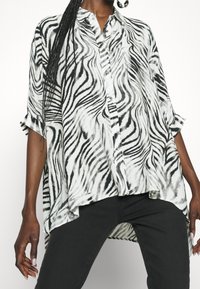 Svart och vit zebra mönstrad knäppskjorta med lös passform, korta ärmar och böjd fåll. Lättviktsmaterial med slät textur.